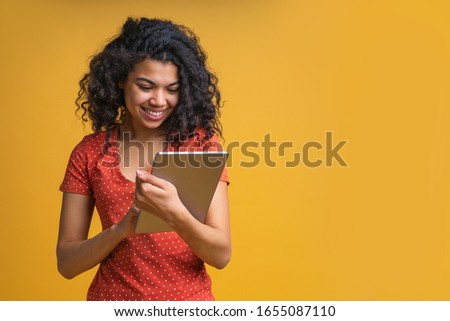 Smiling young casually dressed female entrepreneur working distantly using her tablet. Student girl preparing to exams isolated on bright colored yellow background. Copy space for your text or logo.