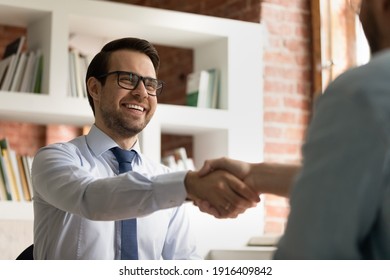 Smiling young Caucasian businessman shake hand of partner or colleague close deal after successful meeting in office. Happy male CEO or employee handshake get acquainted greet with business client.