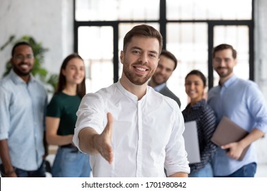 Smiling young Caucasian businessman stretch hand greeting meeting with new office employee or worker, happy male team leader or employer welcome newcomer or intern at workplace, recruitment concept