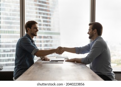 Smiling young Caucasian businessmen handshake get acquainted greeting at meeting in office. Happy male employees colleagues shake hands close deal make agreement after successful negotiation. - Shutterstock ID 2040223856