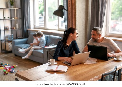 Smiling young Caucasian couple parents work online at home on laptops, sit on lockdown with children. Happy mom and dad freelancers use computers stay indoors on quarantine. Distant job concept. - Powered by Shutterstock