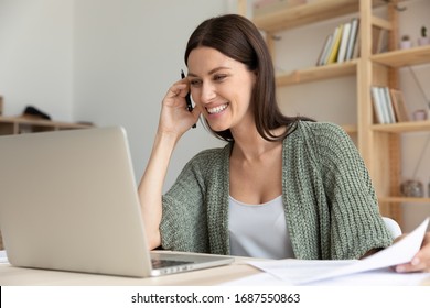 Smiling Young Caucasian Female Employee Sit At Desk Make Notes In Notebook Watching Webinar On Laptop, Happy Woman Worker Laugh Have Fun Enjoying Funny Video Or Call On Computer At Workplace