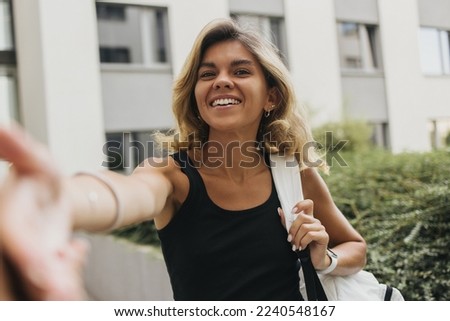 Smiling young caucasian girl with snow-white smile takes selfie outdoors. Blonde wears backpack and casual clothes. Sincere emotions lifestyle concept