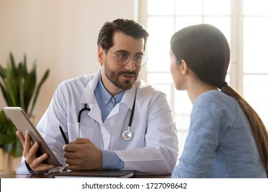Smiling young Caucasian male doctor in white medical uniform consult female patient using tablet on consultation, modern man GP talk discuss checkup results with woman client at meeting in hospital - Shutterstock ID 1727098642