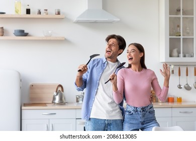 Smiling young caucasian male and female have fun, sing song at microphone, prepare food in kitchen interior. Fun together, couple feeling happy, enjoying weekend free time, positive mood, lifestyle - Powered by Shutterstock