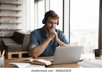 Smiling Young Caucasian Male Student In Earphones Use Computer Study Online From Home. Happy Millennial Man Wear Headphones Have Online Video Lesson Or Webcam Course Or Training On Laptop.