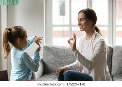 Smiling Young Caucasian Mom And Little Daughter Make Hand Gesture Learn Speak Sign Language At Home, Happy Mother Or Nanny Practice Nonverbal Talk With Small Disabled Girl Child, Disability Concept