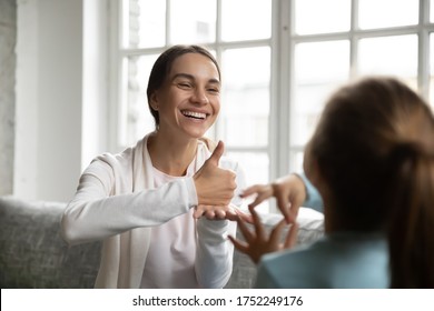 Smiling young Caucasian mom or nanny make hand gesture practice nonverbal talk with little girl child, positive female teacher or tutor learn sign language with small disabled kid, disability concept