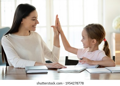 Smiling Young Caucasian Mother And Little 7s Daughter Give High Five For Finished Homework Assignment. Happy Loving Mom And Small Girl Child Celebrate Good Study Result. Education, Learning Concept.