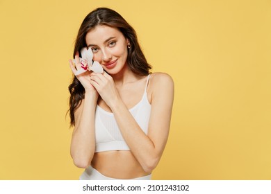 Smiling Young Caucasian Nice Beautiful Brunette Woman 20s Wearing White Underwear Brassiere Hold In Hand Flower Isolated On Plain Yellow Color Background Studio Portrait. People Female Beauty Concept