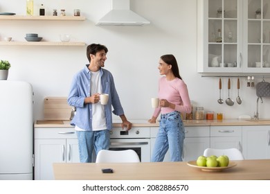 Smiling young caucasian wife and husband with cups talk and drink coffee in morning in minimalist kitchen interior. Breakfast together, morning drink, break, communication and relationship concept - Powered by Shutterstock