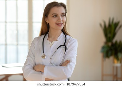 Smiling young Caucasian woman doctor or nurse in white medical uniform look in distance dream or think. Happy female GP or physician consider future medical career perspectives, visualize imagine. - Shutterstock ID 1873477354