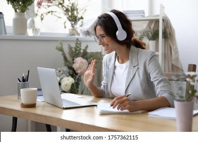 Smiling young Caucasian woman in headphones take online educational course or training on laptop from home, happy female in wireless headset wave to camera, talk on webcam video call on computer - Shutterstock ID 1757362115