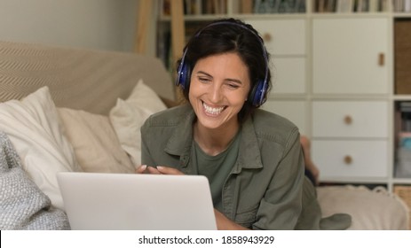 Smiling young Caucasian woman in headphones laugh look at laptop screen have pleasant webcam digital virtual conference. Happy female in earphones talk speak on video call on computer at home.