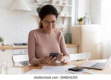 Smiling young Caucasian woman manage household budget finances paying bills taxes on smartphone online. Happy female busy with documents calculate expenses expenditures on cellphone on internet. - Shutterstock ID 2048241353