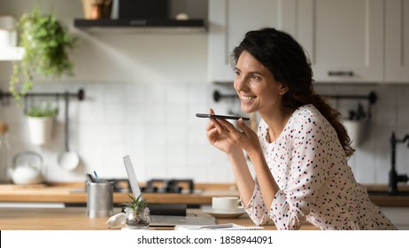 Smiling Young Caucasian Woman Record Audio Message On Modern Smartphone Gadget At Home Office Kitchen. Happy Female Activate Digital Voice Recognition Application On Cellphone. Technology Concept.