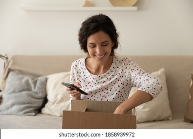 Smiling young Caucasian woman sit on couch at home unpack post box shopping online on smartphone form home. Excited female buyer unbox package with internet order. Good delivery service concept. - Powered by Shutterstock