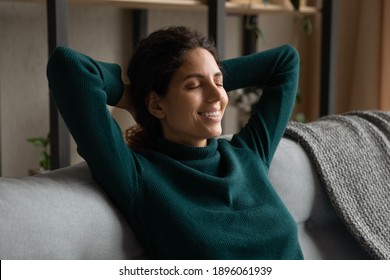 Smiling young Caucasian woman sit rest on sofa in living room with eyes closed sleeping or dreaming. Happy millennial female relax on couch at home relieve negative emotions. Stress free concept.