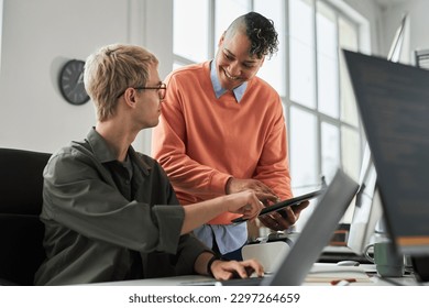 Smiling young colleague consulting with programmer about new software on digital tablet during their work in office - Shutterstock ID 2297264659