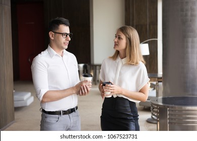 Smiling young colleagues talking at coffee break. Young Caucasian businessman wearing glasses and businesswoman holding takeaway coffee communicating. Business break concept