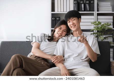 A smiling young couple of boys and girls were sitting on the sofa in the living room, teasing each other with fun.