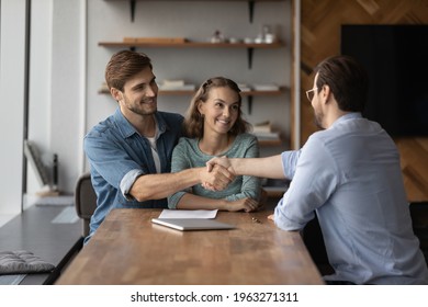 Smiling young couple buyers shake and get acquainted greet with relator or broker at office meeting. Happy man and woman clients handshake close deal or make agreement with real estate agent. - Shutterstock ID 1963271311