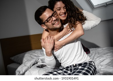 Smiling young couple cuddling while sitting in bed.