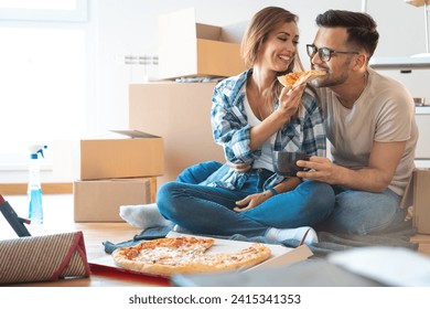 Smiling young couple eating fast food surrounded by cleaning equipment and cardboard boxes in new home. - Powered by Shutterstock