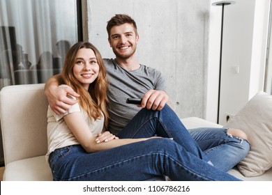 Lächelndes junges Paar umarmt, während es zu Hause auf einer Couch sitzt und fernsieht