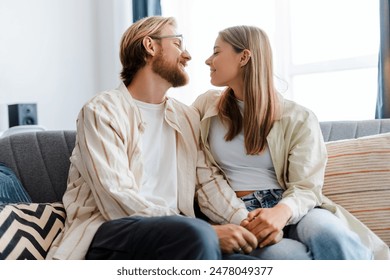 Smiling young couple looking at each other with love while sitting on a couch at home. They are holding hands and enjoying their time together. Relationship concept - Powered by Shutterstock