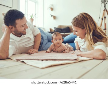 Smiling young couple lying together on blankets on their living room floor at home with their adorable baby daughter - Shutterstock ID 762865441