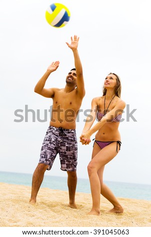 Smiling young couple playing volleyball on the beach. Focus on the woman