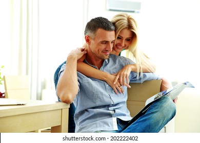 Smiling Young Couple Reading Magazine At Home