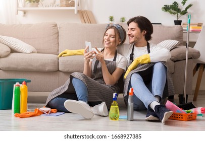 Smiling young couple relaxing with smartphone after spring-clean apartment, sitting on floor with lots of detergents and cleaning supplies, free space - Powered by Shutterstock