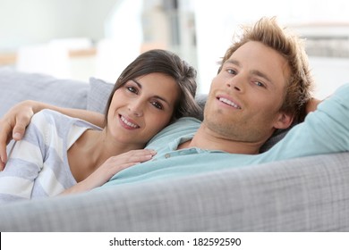 Lächelndes junges Ehepaar, das sich auf dem Sofa zu Hause entspannt