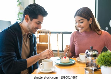 Smiling Young Couple Sharing Dessert At Table In Cafe