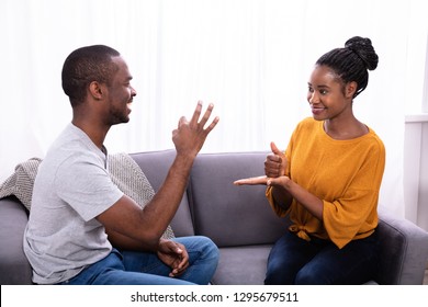 Smiling Young Couple Sitting On Sofa Communicating With Sign Languages