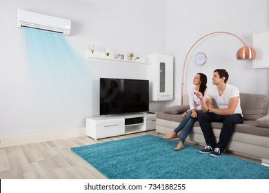 Smiling Young Couple Sitting On Sofa Using Air Conditioner