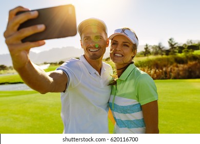 Smiling young couple taking self portrait at golf course. Happy male and female golfers taking selfie with smart phone at field on sunny day. - Powered by Shutterstock