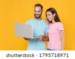 Smiling young couple two friends guy girl in blue pink t-shirts isolated on yellow wall background studio portrait. People lifestyle concept. Mock up copy space. Working on laptop pc computer hugging.