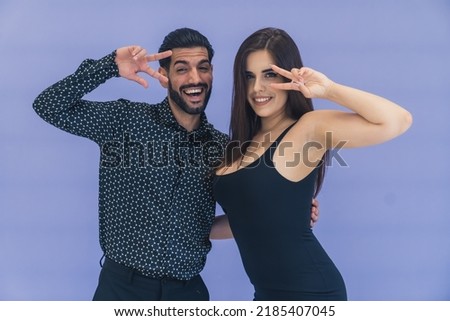 Smiling young couple wearing dark clothes posing for picture with peace signs in front of their faces. Studio shot. High quality photo