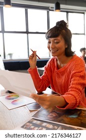 Smiling Young Creative Asian Businesswoman With Photograph At Desk In Office. Unaltered, Creative Business, Workplace, Photography Themes.