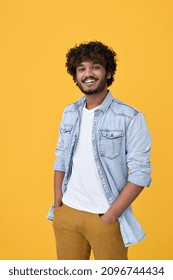 Smiling Young Curly Indian Cool Positive Guy Standing Isolated On Yellow Background. Happy Ethnic Stylish Millennial Man Wearing Blue Casual T-shirt Looking At Camera Posing For Portrait. Vertical