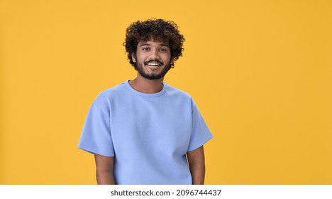 Smiling Young Curly Indian Cool Positive Guy Standing Isolated On Yellow Background. Happy Ethnic Stylish Millennial Man Wearing Blue Casual T-shirt Looking At Camera Posing For Portrait.