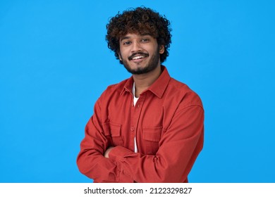 Smiling young curly indian cool guy standing isolated on blue background. Happy ethnic stylish millennial confident man looking at camera posing with arms crossed for portrait.