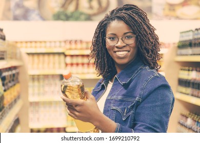 Smiling young customer holding bottle of oil. Cheerful African American woman standing in supermarket and looking at camera. Shopping concept - Powered by Shutterstock