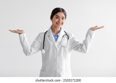 Smiling young cute indian female doctor in uniform show both hands open palms, presenting and advertising comparison and balance isolated over white background. Nurse leaves choice to patient, studio - Powered by Shutterstock