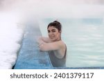 A smiling young dark-haired woman bathes in a hot thermal spring on a winter day.Self-care,healthy lifestyle,leisure activity,mental health concept.