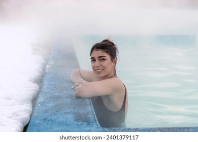 A smiling young dark-haired woman bathes in a hot thermal spring on a winter day.Self-care,healthy lifestyle,leisure activity,mental health concept. - Powered by Shutterstock