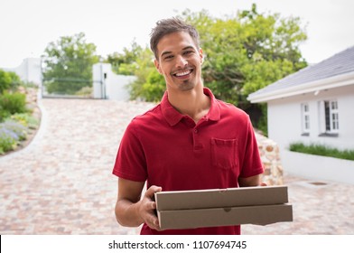 Smiling Young Delivery Man Holding Pizza Boxes Outdoor. Happy Deliveryman In Red T-shirt Holding Two Pizzas Outside House. Portrait Of Satisfied Guy Delivering Pizzas And Looking At Camera.